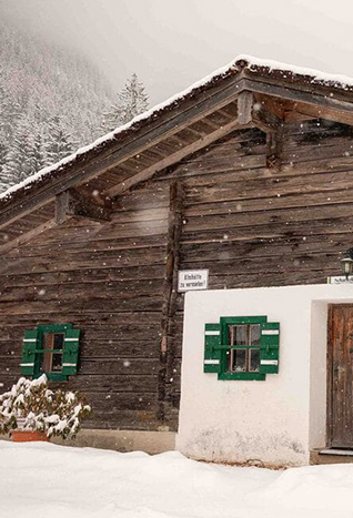Schneebedeckte Holz-Almhütte mit grün lackierten Fensterläden