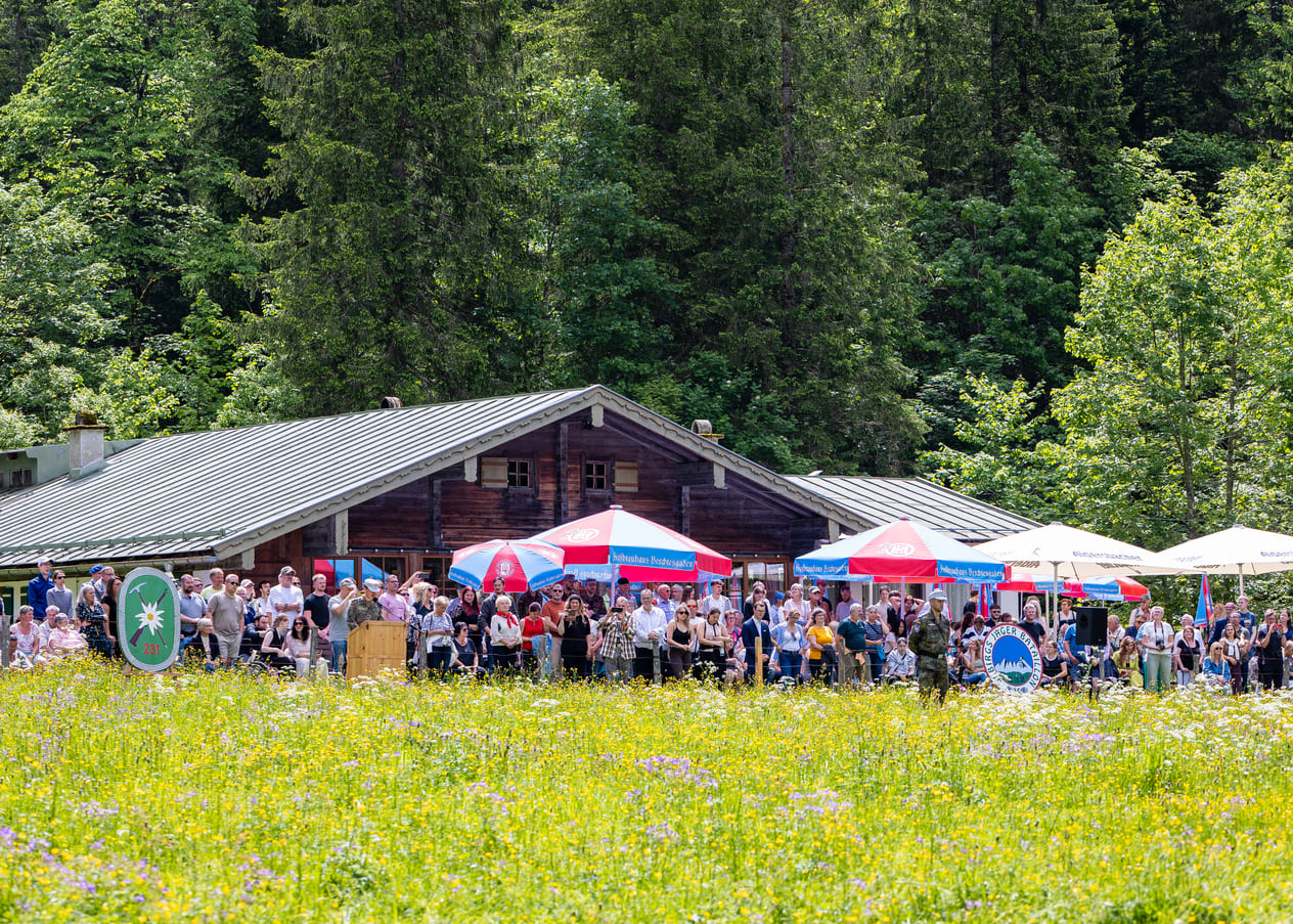 Große Menschenmenge vor einer rustikalen Almhütte mit bunten Sonnenschirmen,