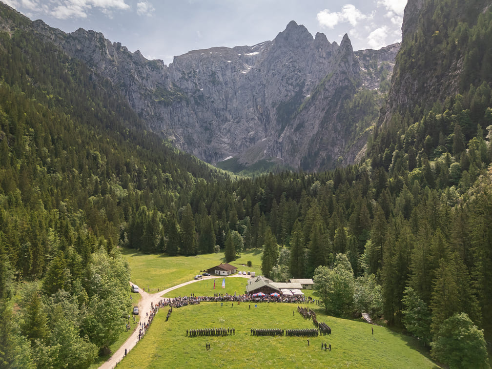 Scharitzkehlalm: weite grüne Almwiese mit Reihen von Menschen und mehreren Hütten